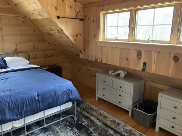 A bedroom with a bed, a dresser, a nightstand, a window, and a wooden ceiling.