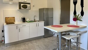 A modern kitchen with white cabinets, a stainless steel refrigerator, a microwave, and a sink. There are two bar stools and a small table with red placemats.