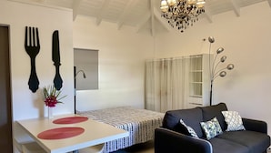 A modern living room with a black sofa, a white dining table, and a chandelier.