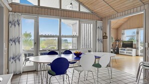 Ett rymligt matområde med ett stort bord och stolar, stora fönster med gardiner och utsikt över omgivningarna.