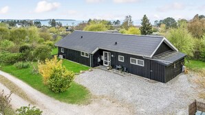Ett svart trähus med en grusuppfart och utsikt över havet.