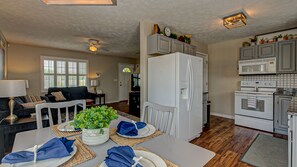 A modern kitchen with white appliances, a dining area with a table set for four, and a living room with a sofa and TV.