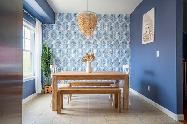 A dining area with a wooden table and benches, a hanging light fixture, a potted plant, and a patterned wall.
