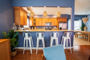 A modern kitchen with wooden cabinets, a central island with bar stools, and hanging pendant lights.