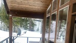 A covered porch with a gray sectional sofa, wooden flooring, and large windows offering a view of a snowy landscape. - Custom Built Home in 2018 Center of Government Camp (Government Camp)