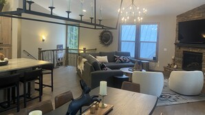 A modern living room with a fireplace, a dining area with a chandelier, and a large window. - Custom Built Home in 2018 Center of Government Camp (Government Camp)