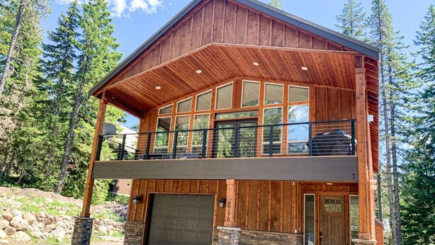 A two-story wooden cabin with a balcony, stone foundation, and large garage doors. - Custom Built Home in 2018 Center of Government Camp (Government Camp)