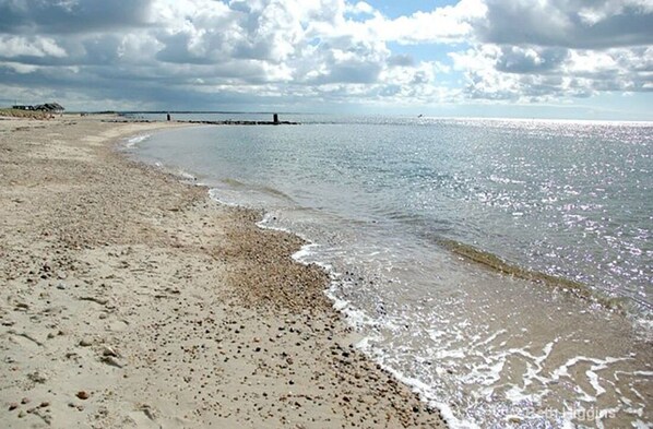 Une plage de sable fin aux vagues douces, un ciel dégagé et une jetée qui se profile à l’horizon.