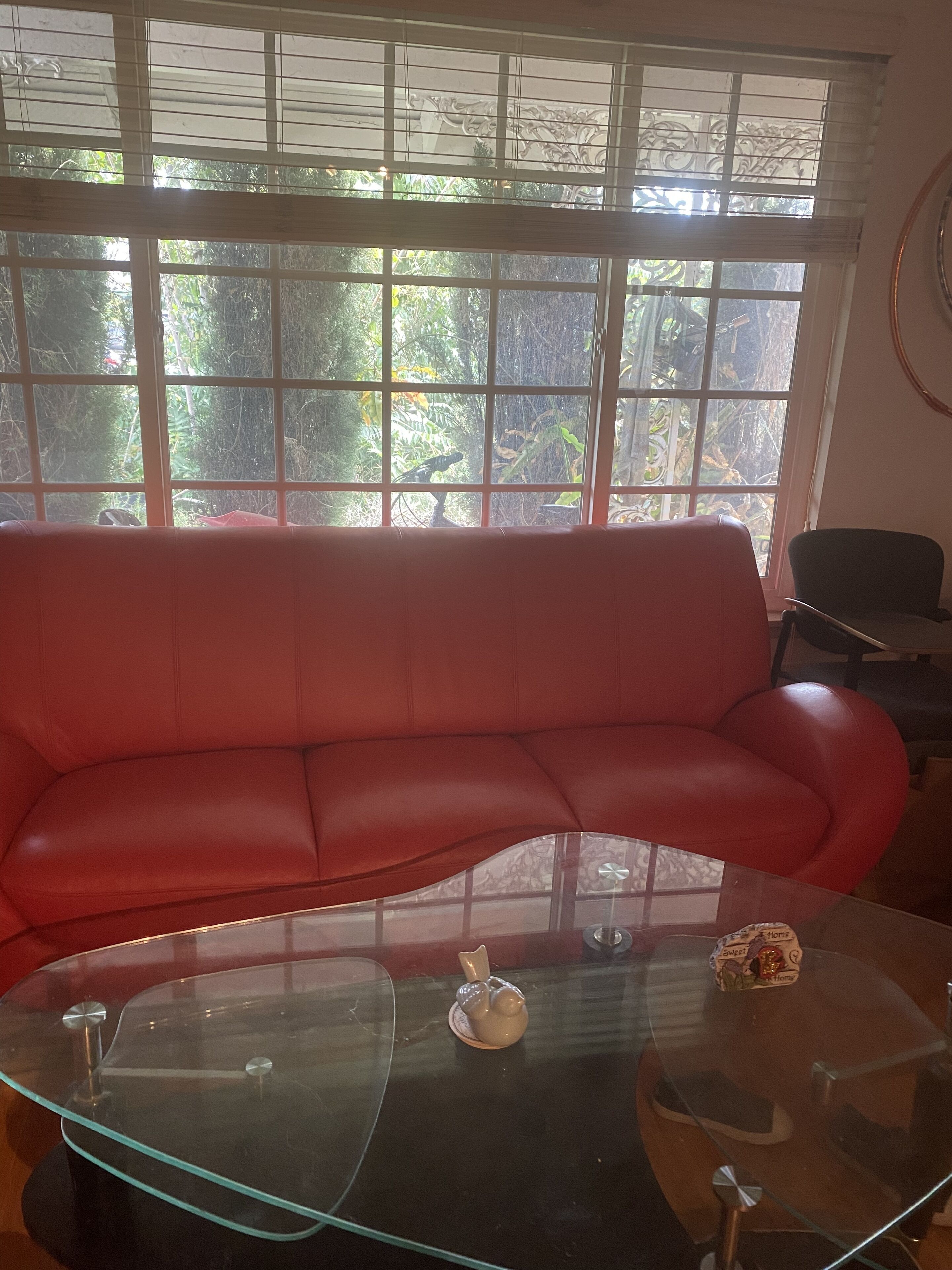 A red leather sofa in a room with a glass coffee table and a view of greenery through large windows.