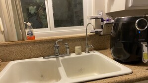 A kitchen with a double sink, a coffee maker, and a window with a view of a plant. - Cozy Peaceful Convenient Sweet Home 1 minute to all places 優雅方便，私用衛浴， 高速出口一分鐘。 (Hacienda Heights)