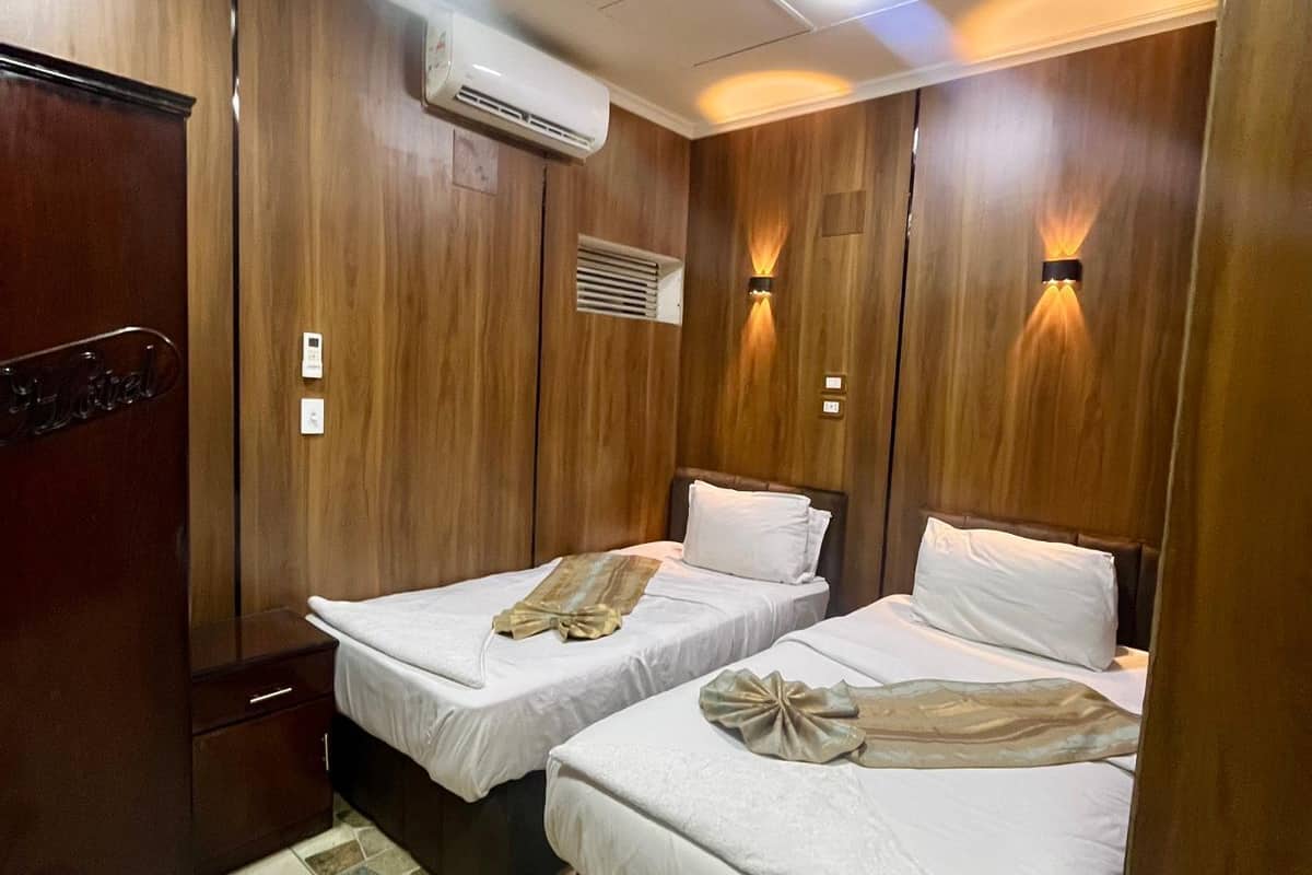 Habitación de hotel con dos camas, un armario, un equipo de aire acondicionado y piso de baldosas.