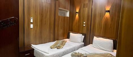 A hotel room with two beds, a wardrobe, an air conditioning unit, and a tiled floor.