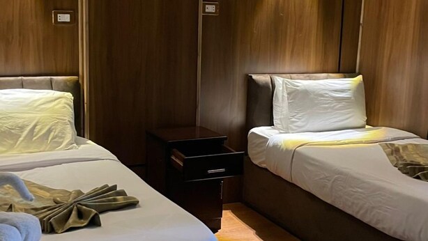 Una habitación de hotel con dos camas, una mesita de noche y una lámpara fijada a la pared.