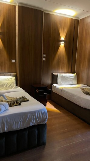 A hotel room with two beds, a nightstand, and a wall-mounted light fixture. - Cairo City (Cairo)