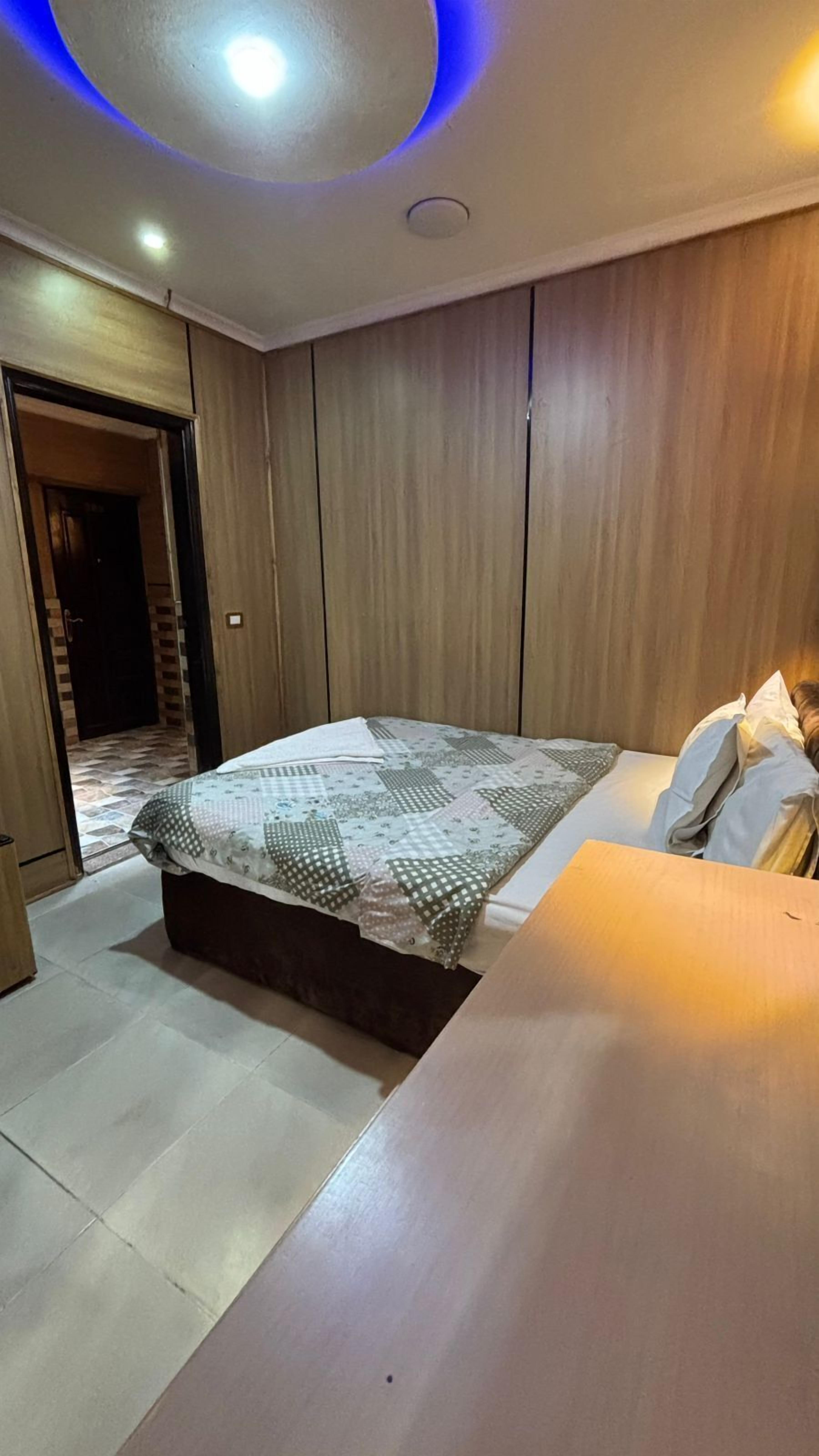A bedroom with a bed, a bedside table, a wardrobe, and a door leading to another room.