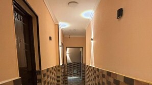Un pasillo con baldosas estampadas, una puerta con número y una lámpara en el techo.