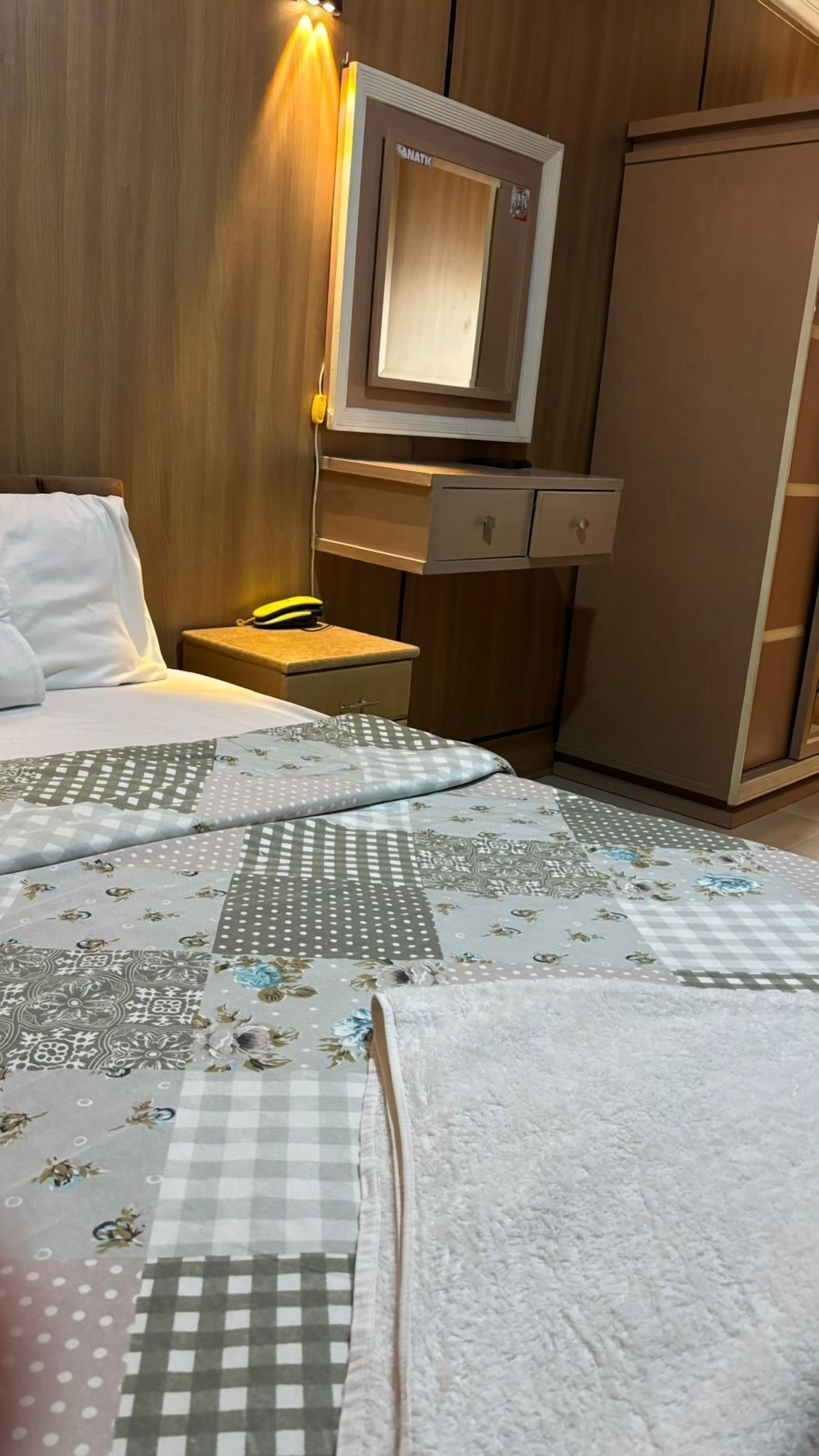 Habitación de hotel con cama, mesita de noche con lámpara, armario y espejo.