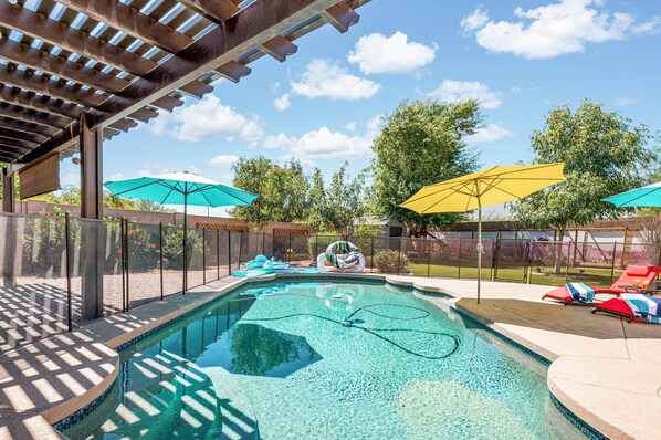 Ein Swimmingpool mit einer Pergola darüber, umgeben von Sonnenschirmen und Liegestühlen.