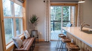 Eine Küche mit Barbereich, Holzstühlen, einer Bank und einem großen Fenster mit Vorhängen.
