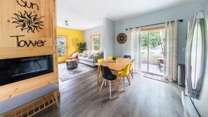 Ein modernes Wohnzimmer mit Kamin, einem Essbereich mit Holztisch und Stühlen sowie einem großen Fenster mit Vorhängen.