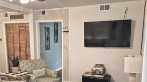 Ein Wohnzimmer mit gemusterten Möbeln, einem Deckenventilator, einem Fernseher und einer Tür mit einer dekorativen Schilder.