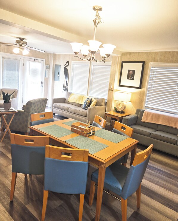 A dining area with a wooden table and blue chairs, a sofa, and a ceiling fan. - First Floor Home, No Stairs, Only One Block From The Ocean (Myrtle Beach)