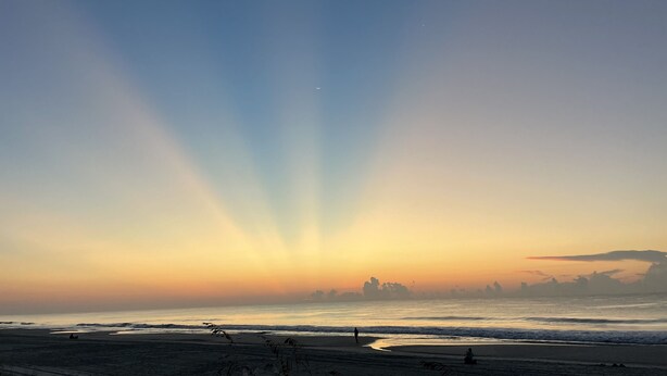 Ein Strand mit Sonnenuntergang, Wellen und einer entfernten Skyline.