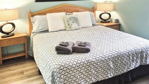 Ein Schlafzimmer mit einem Bett, zwei Nachttischen, einem Deckenventilator und einem gerahmten Kunstwerk an der Wand.