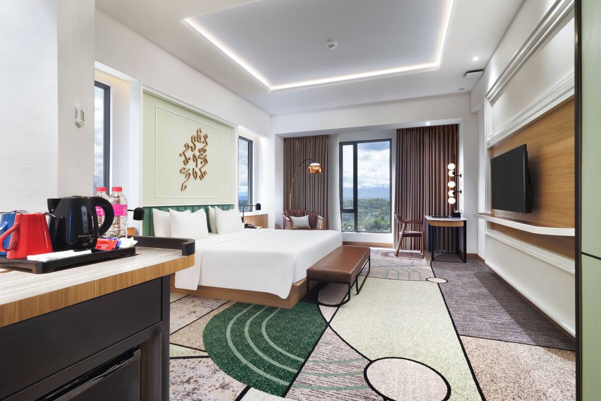 Quarto de hotel com uma cama grande, uma mesa com cafeteira, uma televisão e vista para o exterior.