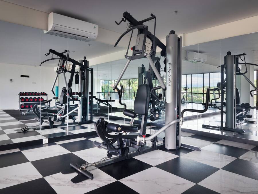 A gym with various exercise machines, a rack of dumbbells, and large windows.