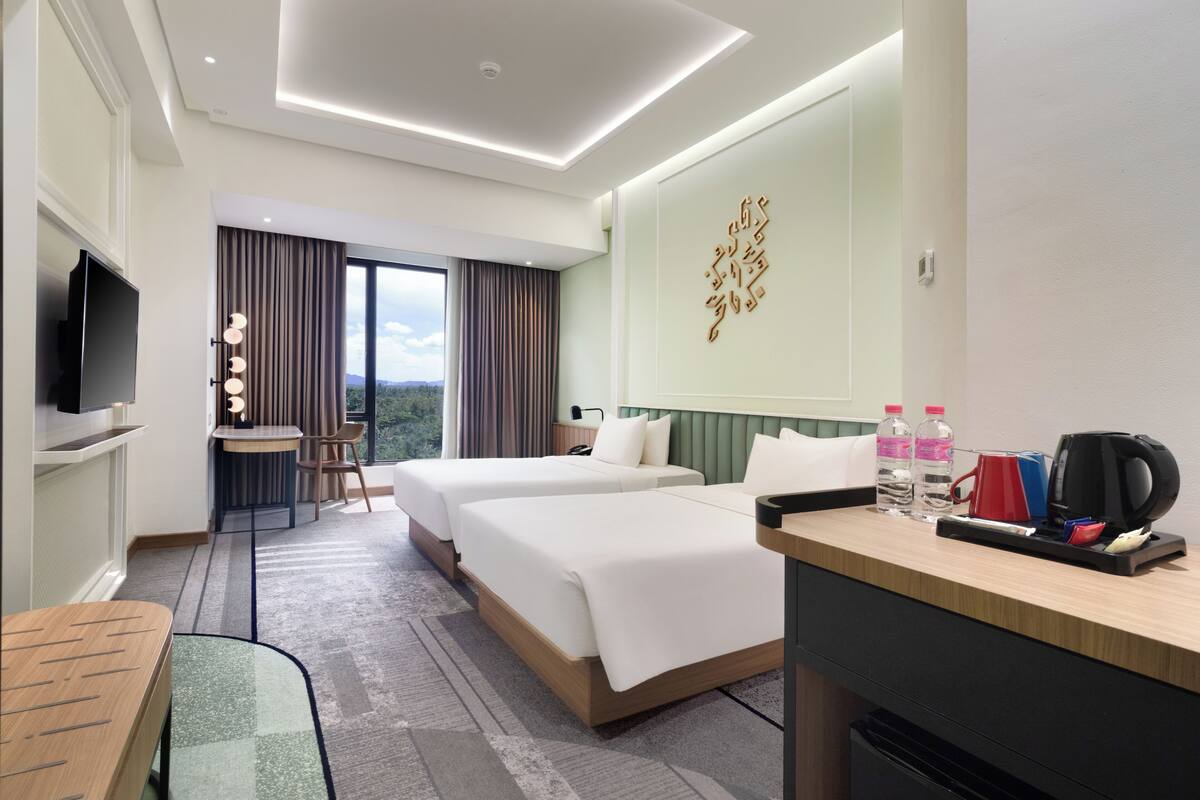 Quarto de hotel com duas camas, uma escrivaninha com máquina de café, garrafas de água e uma televisão.