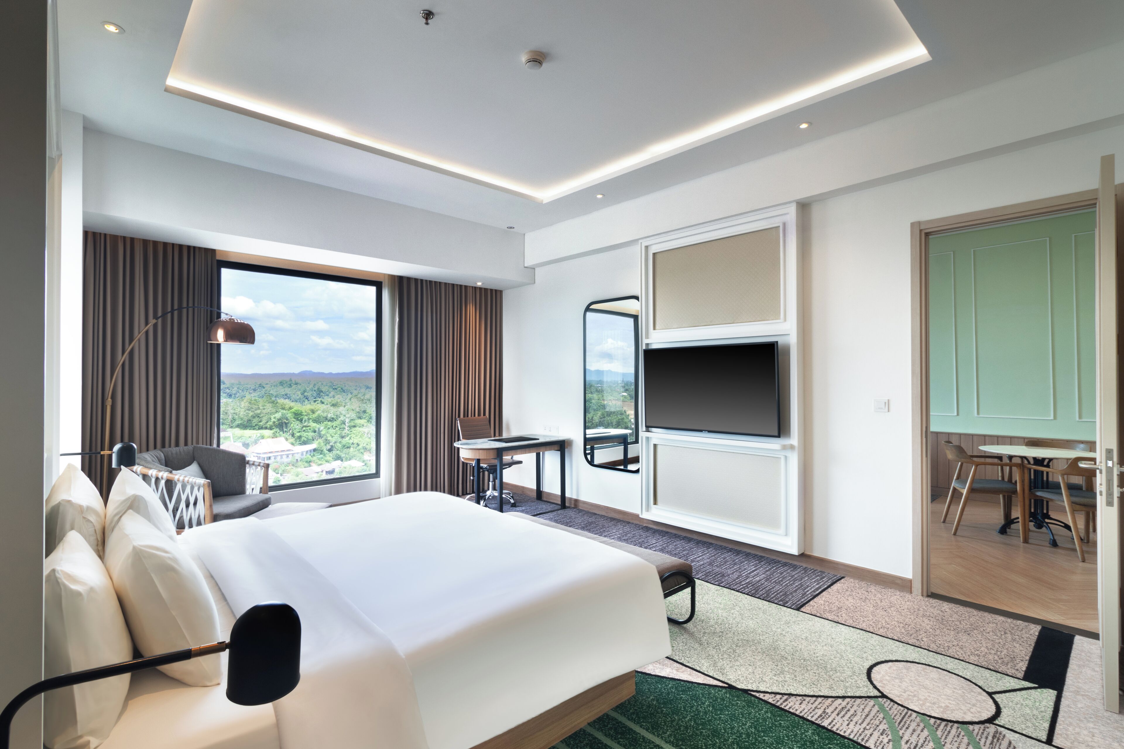 A hotel room with a large bed, a desk, a chair, a TV, and a view of the outdoors.