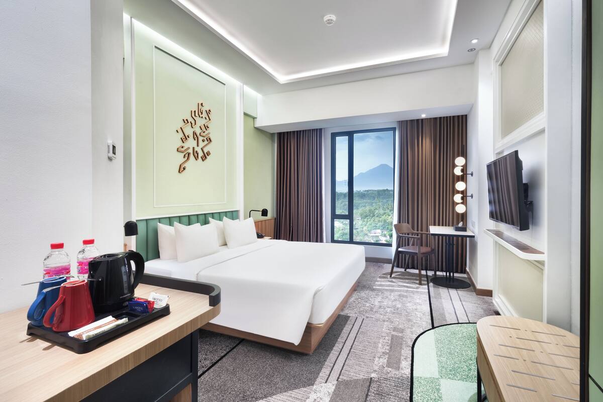 Quarto de hotel com uma cama grande, uma mesa com cadeira, uma televisão e vista para uma montanha.