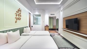 A hotel room with two beds, a TV, a mirror, and a bathroom visible through a glass door.