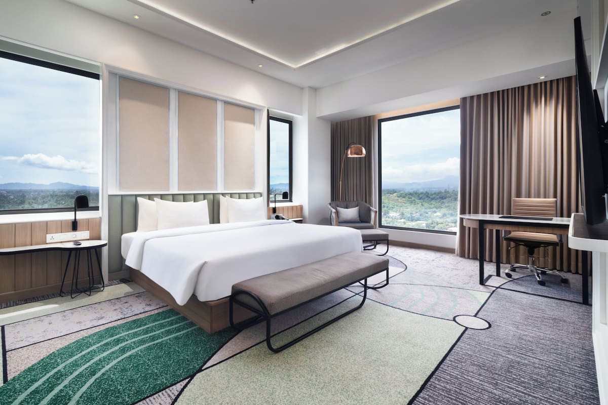 Quarto de hotel moderno com uma cama grande, uma escrivaninha, uma cadeira e vista para as montanhas.