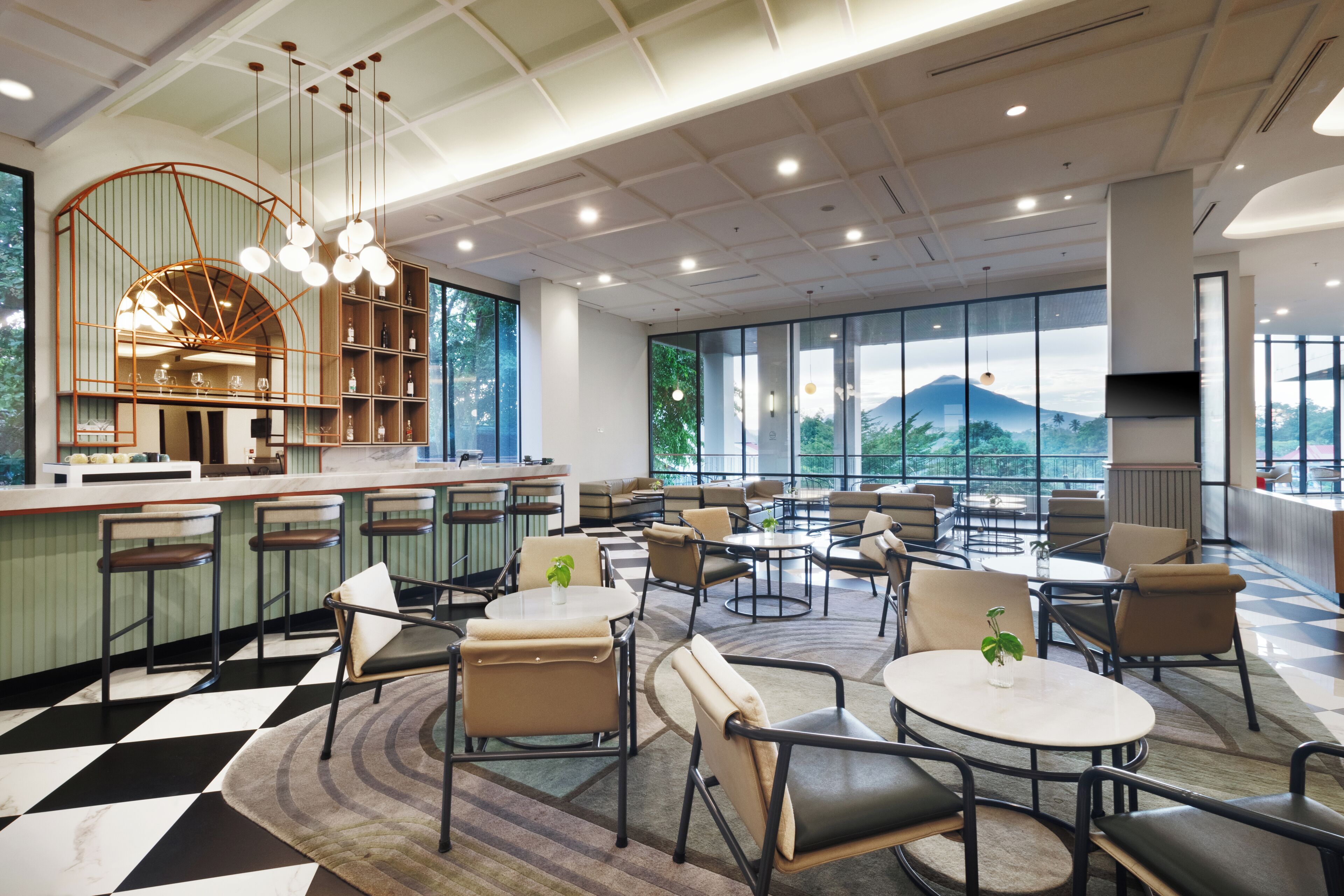 A modern hotel lobby with a checkered floor, seating areas, a bar, and large windows offering mountain views.