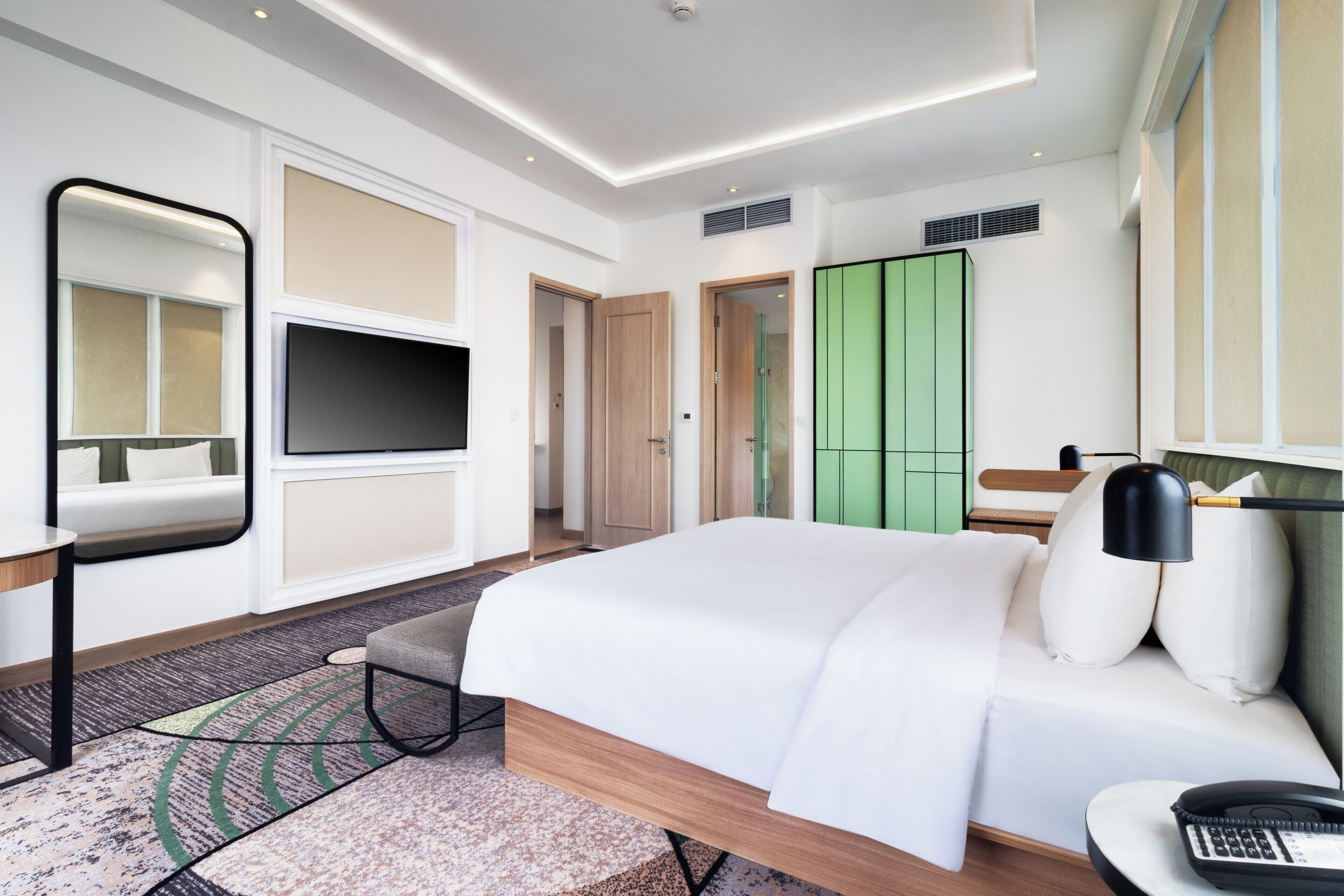 Une chambre d’hôtel moderne avec un grand lit, une télévision, un bureau et une armoire verte.