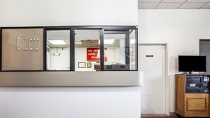 Un espace d’accueil avec une cloison en verre, un meuble en bois abritant un téléviseur, et un tapis rouge orné du logo EconoLodge.