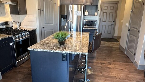 A modern kitchen with a central island, stainless steel appliances, and a wooden floor. - Three Bedroom House,  sleeps 7 (Edmonton)