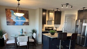 A modern kitchen with dark cabinetry, stainless steel appliances, and a central island with bar stools. - Three Bedroom House,  sleeps 7 (Edmonton)