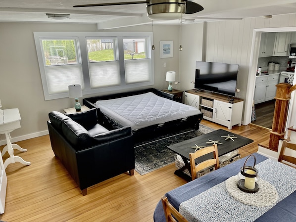A modern living room with a large bed, a sofa, a dining area, and a TV.