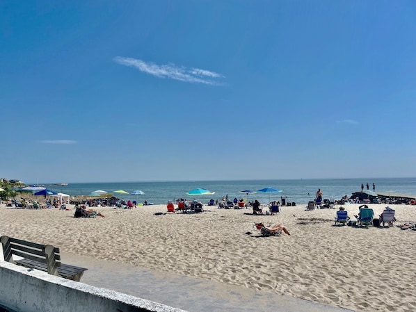 A beach with sun loungers and umbrellas, a wooden bench, and a clear sky.