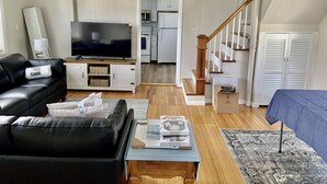 A living room with a black leather sofa, a flat-screen TV, a wooden coffee table, and a blue tablecloth. - Beach Ready 3-bdrm house, Short Walk to Private Beach and Park, Lots of Parking (Niantic)