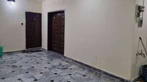 Um corredor com duas portas de madeira, piso de azulejos e um acessório de iluminação no teto.