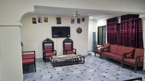 Uma sala de estar com sofá, cadeiras, televisão e tapete estampado.
