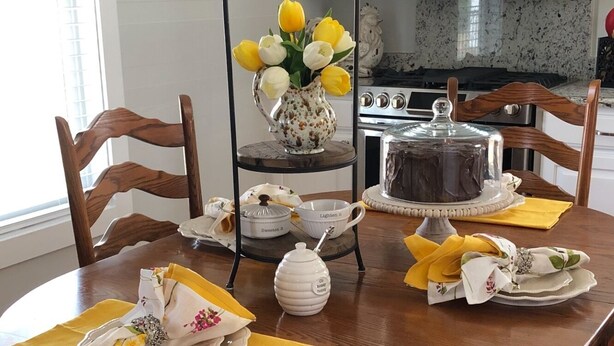A dining table set with a cake, teapot, cups, and a vase of flowers. - The White Magnolia Cottage (Round Top)