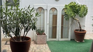 A courtyard with potted plants, a small garden area, and a white building with arched windows.