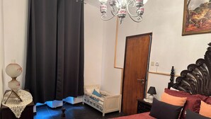 A bedroom with a bed, a nightstand, a lamp, a chandelier, a door, and a painting on the wall.