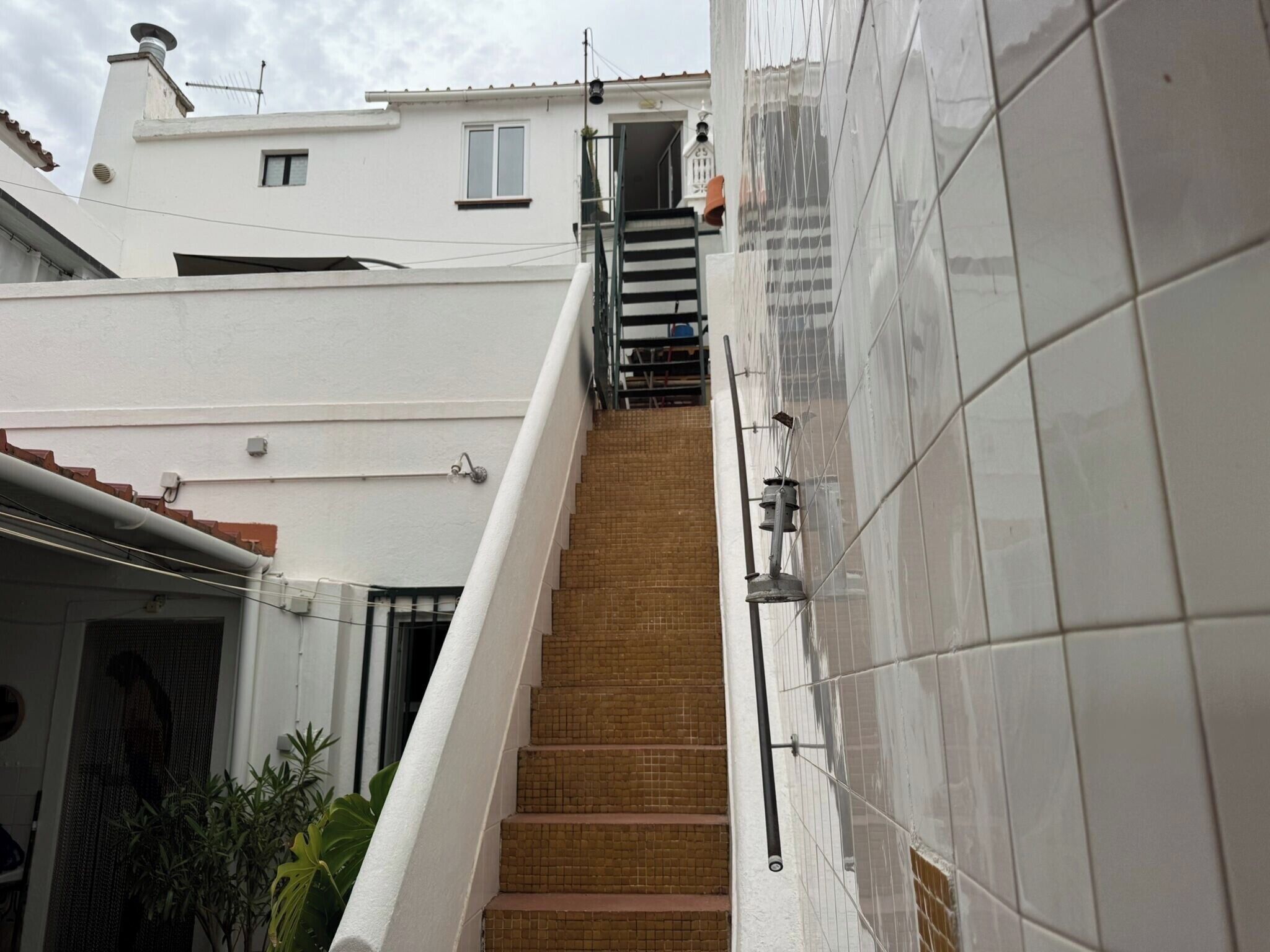 Eine Treppe führt zu einer Tür, ausgestattet mit einem Metallgeländer, einer gefliesten Wand und einem kleinen Fenster am Gebäude.