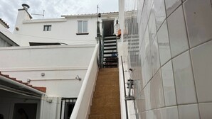 A staircase leading to a door with a metal handrail, a tiled wall, and a small window on the building.